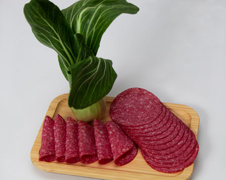 Round pieces of salami accompanied by asian cabbage on a wooden board with a white backgroundの写真素材