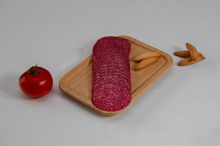 Salami with a very fresh tomato and some thick bread on a wooden board with a white backgroundの写真素材