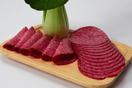Round pieces of salami accompanied by asian cabbage on a wooden board with a white backgroundの写真素材