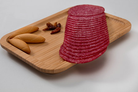 Wheels of salami with pieces of bread and cayenne on a wooden board with a white backgroundの写真素材