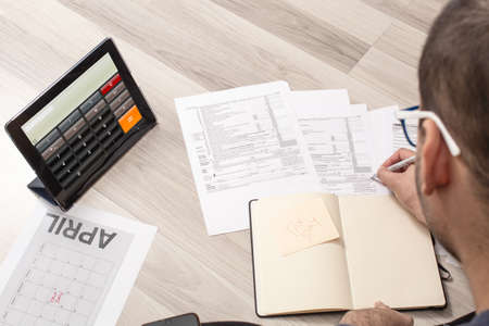 Caucasian man in casual clothes calculating taxes on the tax dial to refund moneyの写真素材