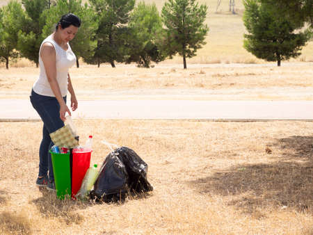 Woman in the forest recycling waste next to recycle cans with plastic cardboard and aluminum the red green and black cansの写真素材