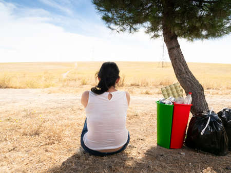 Woman in the forest recycling waste next to recycle cans with plastic cardboard and aluminum the red green and black cansの写真素材