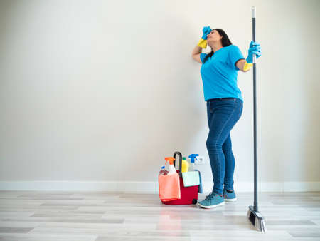 Caucasian young woman cleaning with a bottle of water brush and broom her house with cleaning gloves and handkerchiefsの写真素材