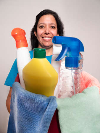 Caucasian young woman in a blue shirt and blue gloves holding a cleaning bottle with cleaning supplies in which are colored handkerchiefs white sprayの写真素材