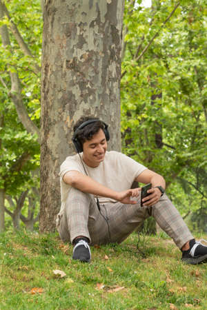 Hispanic brunette boy listening to music with headphones and yellow clothes in a green forest smilingの写真素材