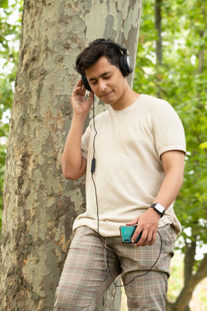 Hispanic brunette boy listening to music with headphones and yellow clothes in a green forest smilingの写真素材