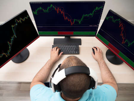 Young caucasian man in a blue shirt sitting with a table and a computer with 3 monitors doing...