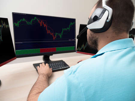 Caucasian young woman sitting at a table doing stock trading on a computer with three black monitors...