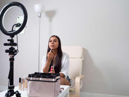 Hispanic young man creating clothing content for social networks with a camera on a tripod, sitting on a piece of furnitureの写真素材