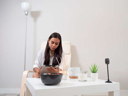 Young woman at home tired from work with a tablet sitting on a chair with a table in front of her in a relaxed atmosphere and drinking teaの写真素材