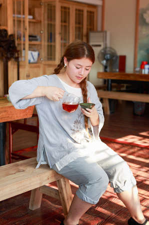A girl dressed in traditional clothing sitting on wooden benches  is drinking teaのeditorial素材