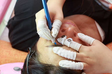 Eyebrows tattooed, a girl is doing a tattoo eyebrow to a customer.