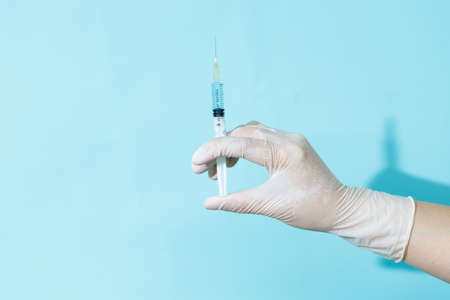 A gloved doctor holds a syringe on a blue background