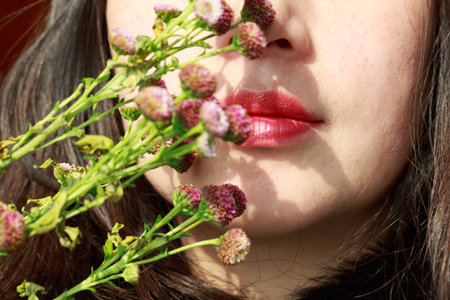 Beautiful young woman with flowers in her mouth. Close-up.の写真素材