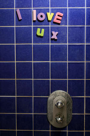 I Love U x written in colorful foam letters on shower. Message left for a lover. The tiles and shower controls are caked with limescale.の写真素材