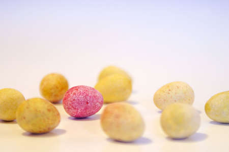 Mini candy chocolate eggs - all yellow except one, in focus, which is speckled red.の写真素材