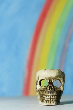 Human skull with a blue sky and rainbow background, a symbol of death, horror and vanitas; portrait format.の写真素材