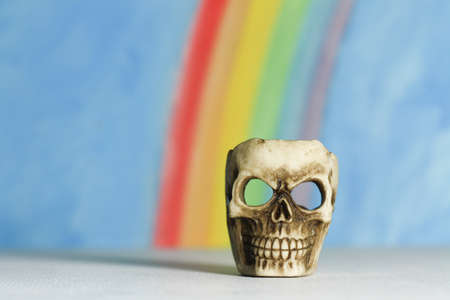 Human skull with a blue sky and rainbow background, a symbol of death, horror and vanitas; landscape format.の写真素材