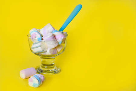 sweet marshmallows in glass with a blue spoon, in a yellow background, with copy spaceの写真素材