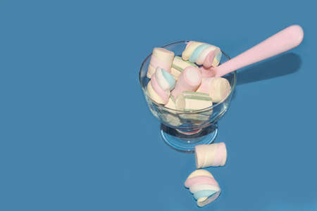 Sweet colored marshmallows with a pink spoon in a glass on blue background with copy spaceの写真素材