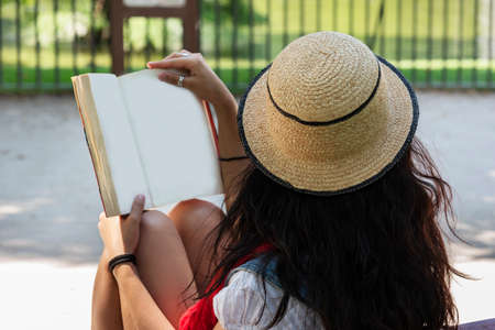 Beautiful young lady reading a book, sitting on a bench in the park. Relaxed concept