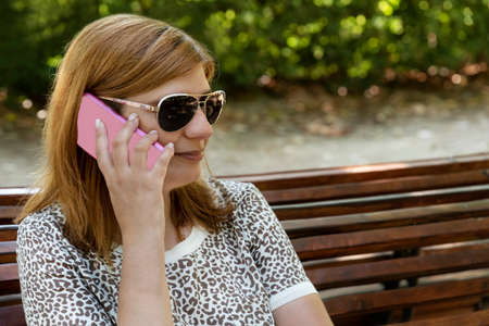Beautiful young woman using her mobile sitting in a bench in the park.の写真素材
