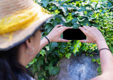 Beautiful young woman with a straw hat, taking a selfie in the park.の写真素材