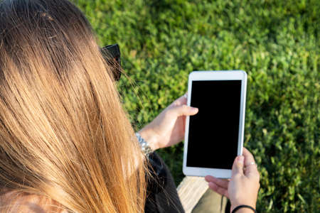 Beautiful young girl using a tablet at sunset, in the park. Relaxing concept.の写真素材