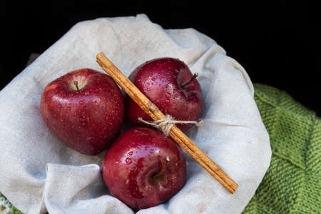 Healthy and organic red apples in a wicker basket and a stick cinnamon on black background with copy spaceの写真素材
