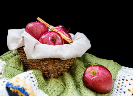 Healthy and organic red apples in a wicker basket and a stick cinnamon on black background with copy spaceの写真素材