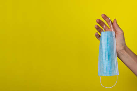 A young woman holds a medical face mask in her hand. Protective mask on a yellow background in the girls hand. Health care conceptの写真素材