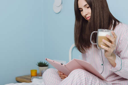 Close up side view portrait of young smiling woman enjoying web surfing using digital tablet, start new day with cup of hot aromatic coffee latte. Millenial freelance girl holds mug good start new dayの写真素材