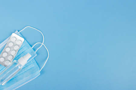 Flat lay pack of white pills,medical face mask and antiseptic on the light blue background. Medicine and health care concept. Copy space for text or design. Infection, virus and influenza protectionの写真素材