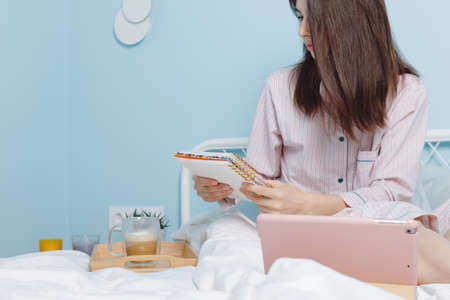 Close up view of beautiful millienial brunette girl sitting on bed, reading her dairy, checking...