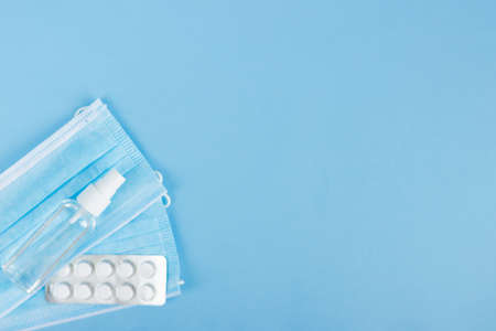 Flat lay pack of white pills,medical face mask and antiseptic on the light blue background. Medicine...