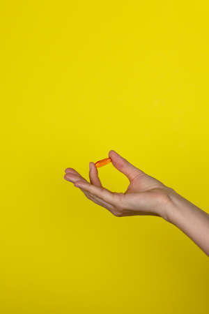 The drug in the girl's hand. A young woman holds an orange medicine capsule in her hand. Copy space for text or design. Vitamin on a yellow background. Health care concept.の写真素材