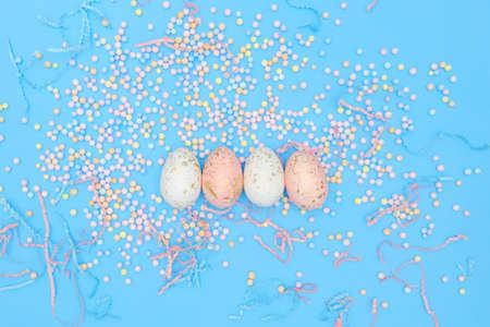 Minimal easter concept. Flat lay composition of four eggs with colorful foam balls, confetti on blue...
