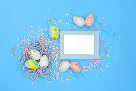Minimal easter concept. Flat lay composition of Easter eggs, colorful foam balls, confetti on blue backdrop, mint frame with space for text, top view. Modern design template of postcard, bannerの写真素材