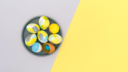 Top view of easter holiday yellow and gray backdrop with creative eggs set on concrete plate in trendy blue, gray, golden colors. Flat lay with copy-paste for text for postcard, banner, invitationの写真素材
