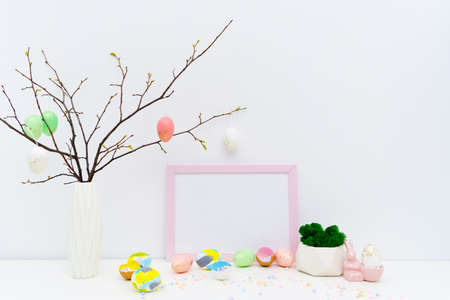 Front view of Easter holiday composition. Hand painted colorful eggs in trendy colors, geometric vase with moss, confetti in eggshell, twigs, pink Easter bunny. Photo frame mockup for Easter designの写真素材