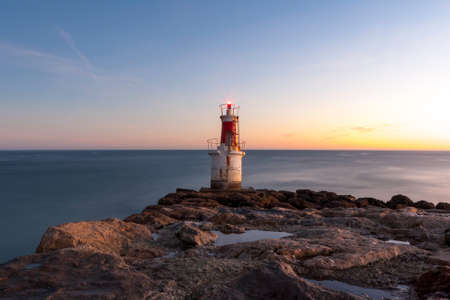 lonely lighthouse illuminated at sea at dawnの写真素材