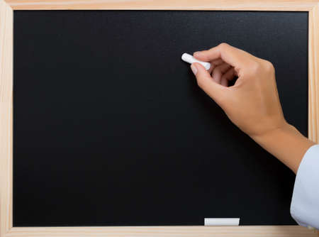 hand holding a white chalk writing on a blackboardの写真素材