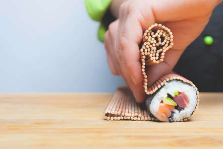 closeup of chef hands rolling up sushi on a bamboo matの写真素材