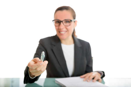 young business woman offering a pen to sign a document sitting on a desk - focus on the penの写真素材