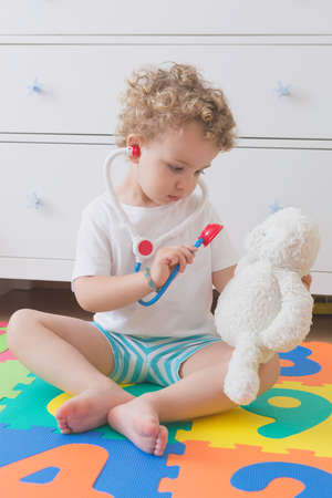 sitting child playing to be a doctor with a toy stethoscope and a teddy bear