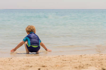 crouched child playing with the water on the seashore his back to the camera - focus on the childの写真素材