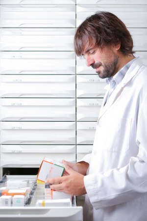 portrait of a smiling young male pharmacist taking a box of medicaments from a drawer - focus on the faceの写真素材