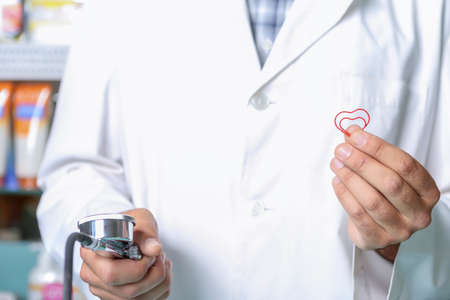 closeup of the hands of a pharmacist with a sphygmomanometer in one hand and a heart red clip shape in the other oneの写真素材