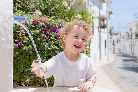 smiling child playing with the water from a fountain on a hot summer day in Altea - Alicante - Valencian Comunityの写真素材